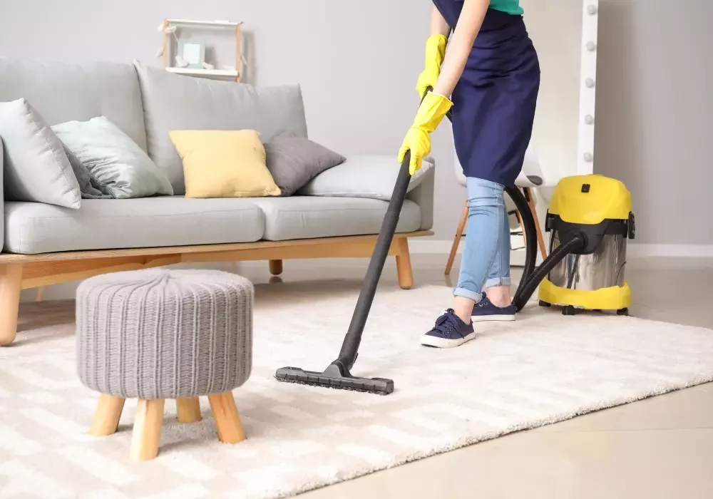 A cleaner vacuums a rug in a living room to prepare a flat for end of tenancy.