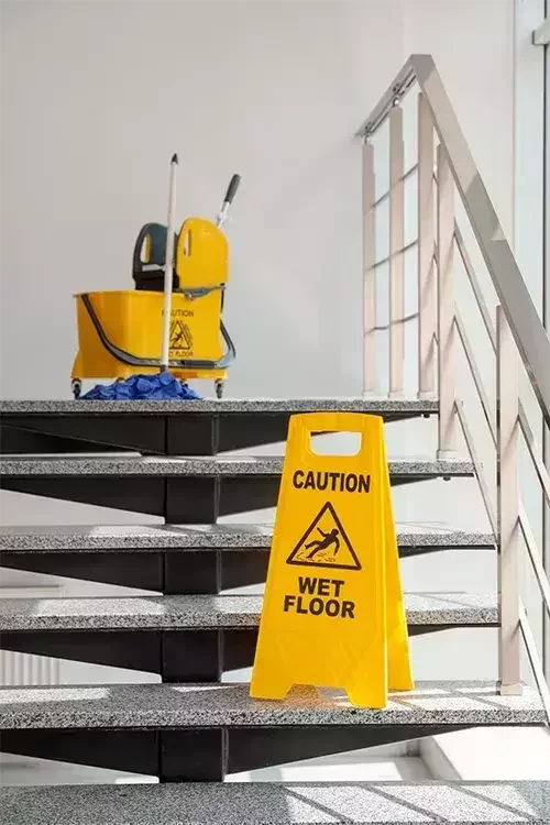 Wet floor sign on staircase with mop and bucket.