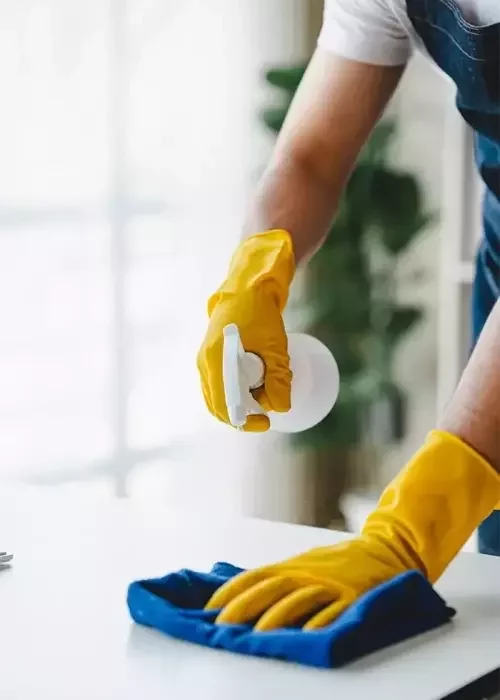 Cleaner wiping down an office table with spray and cloth.